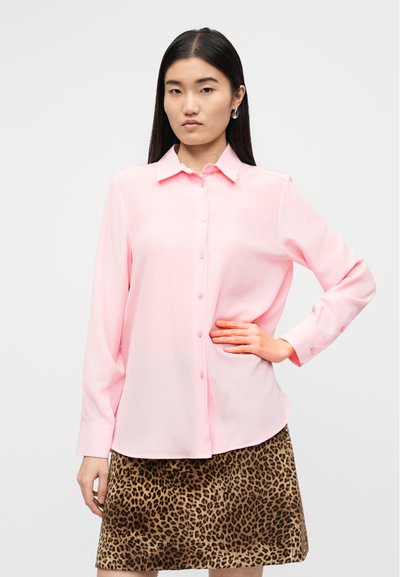 Ανοιχτό ροζ μπλούζα με κουμπιά, γιακά και μακριά μανίκια, φορεμένη πάνω από φούστα με λεοπάρ τύπωμα. Λείο, ελαφρύ ύφασμα, εφαρμοστή γραμμή.