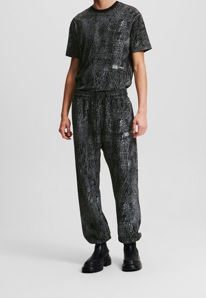 Man wearing black and gray cracked-pattern matching t-shirt and jogger pants with black chunky boots, standing against plain background.
