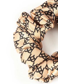 Scrunchie gemaakt van beige satijnen stof met een zwart geometrisch patroon. Het heeft een zachte, gladde textuur en een geplooid ontwerp.