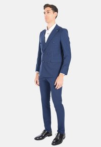 Completo blu navy con righe, giacca doppiopetto, pantaloni slim-fit e scarpe eleganti nere lucide. Camicia bianca sotto.