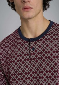 Camicia a maniche lunghe rossa con motivo geometrico, dotata di colletto blu navy e due bottoni scuri all'icollo.