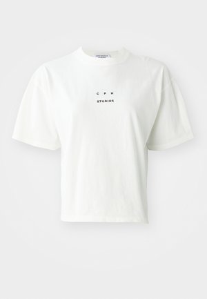 T-shirt blanc court en coton, avec des manches courtes, un col rond et un logo noir imprimé qui indique "CPH STUDIOS" sur le devant.