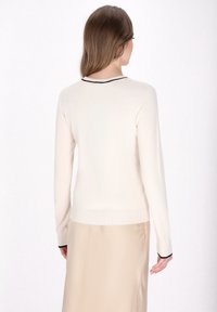 Beżowy sweter z długim rękawem, dopasowany fason, czarne wykończenie przy dekolcie i prążkowany dół. Miękka tekstura, smukła sylwetka i minimalistyczny styl.