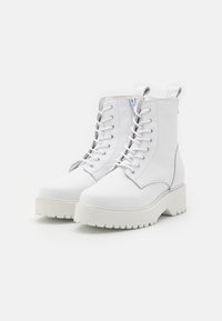 Bottines blanches en cuir texturé, dotées d'une semelle plateforme épaisse, d'un bout rond, d'un laçage à l'avant avec œillets en métal et d'une fermeture éclair sur le côté.