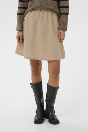 Beżowa spódnica do kolan z elastyczną talią, noszona z czarnymi skórzanymi kozakami sięgającymi do połowy łydki oraz brązowym swetrem w paski.