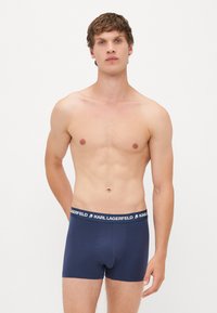 Bóxer de color azul marino con una cinturilla elástica de marca. Fabricado con una tela suave y lisa, con un diseño ajustado y sin patrones visibles.