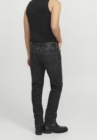 Svarta denimjeans med smal passform, med femficksdesign och synlig sömnad. Bärs med ett svart bälte och ankelstövlar.