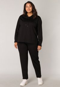 Zwarte hoodie met een koord en lange mouwen, gecombineerd met bijpassende zwarte broek. Beide items hebben een zachte, gladde textuur.