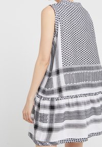 Vestido sin mangas de patrón en blanco y negro que presenta varias texturas y diseños, incluidos formas geométricas y rayas horizontales.