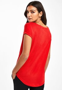 T-shirt rouge à manches courtes avec un col rond et une coupe décontractée, présentant une texture lisse et un ourlet légèrement incurvé à l'arrière.