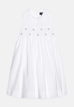 Robe blanche sans manches avec col Peter Pan, corsage smocké et petite broderie florale rose sur la poitrine, jupe fluide en bas.
