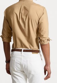 Ljusbeige långärmad skjorta med rullade manschetter, veckdetalj på baksidan, ihopparad med vita jeans och ett brunt läderbälte.