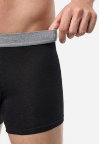 Schwarze Boxershorts aus dehnbarem Baumwollmischgewebe, mit einem grauen gestrickten Bündchen, das den eingeprägten Markennamen trägt.