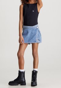 Un body sin mangas negro combinado con una falda envolvente de mezclilla azul clara con botón lateral y bordado de logo. Botas de combate negras con calcetines blancos.