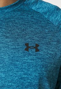 Tyrkysové sportovní tričko vyrobené z texturované látky, s černým logem Under Armour na hrudi a designem s kulatým výstřihem.