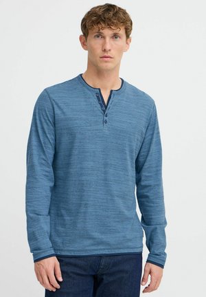 Long-sleeve, blue henley shirt with textured fabric, three-button placket, and contrasting collar trim. Paired with dark denim jeans.