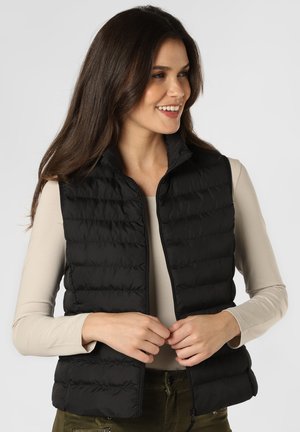 Zwarte opblaasbare vest met hoge kraag, ritsluiting en horizontale stiksels. Lichtgewicht materiaal, gedragen over een beige lange mouwen shirt.