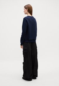 Felpa girocollo blu navy e pantaloni cargo neri con tasche con zip. Tessuto liscio con una vestibilità comoda e dettagli arricciati sui pantaloni.