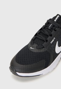 Baskets noires avec une tige en mesh texturé, des lacets plats, un logo Nike blanc et une semelle intermédiaire blanche rembourrée, conçues pour le confort et le soutien.