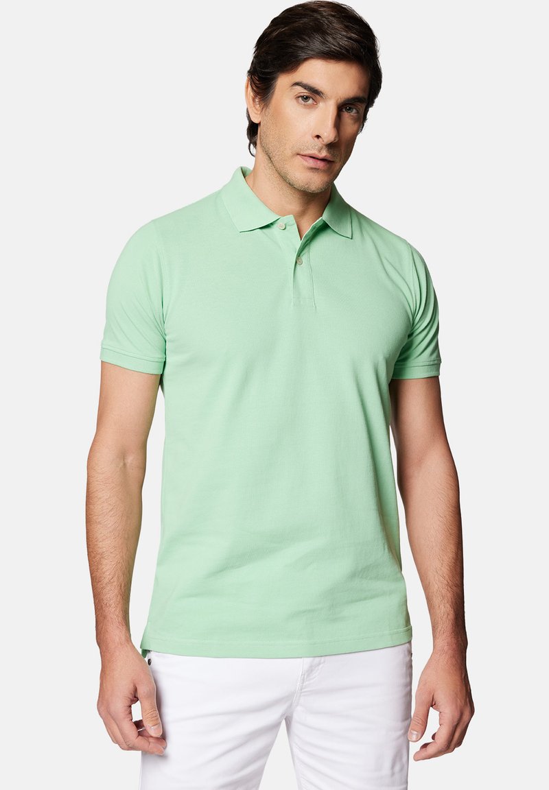Miętowa koszulka polo wykonana z gładkiej bawełny, z krótkimi rękawami, kołnierzykiem i zapięciem na trzy guziki. Noszona z białymi spodniami.