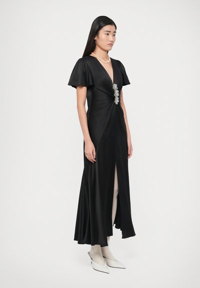 Fekete szatén ruha rövid, fodros ujjakkal, csavart elülső résszel és dekoratív brossal a deréknál. Magas hasítékkal a combnál.