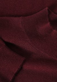 Burgundi színű kötött pulóver részletek, bordázott nyakkal és mandzsettákkal, sima textúrával és letisztult vonalakkal.