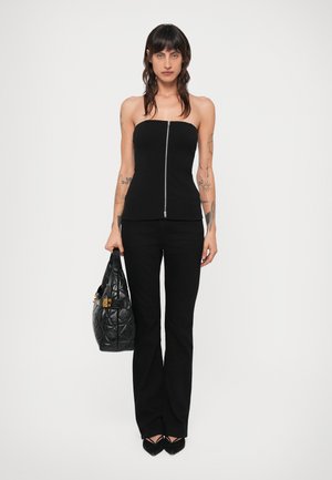 Black strapless top with a front zipper, paired with black flared pants. The model carries a black quilted handbag with gold accents.