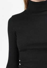 Must taeva musta ribaga kaelusega topp pikkade varrukatega. Kangas on sile ja veniv, sobitudes tihedalt kehale ilma lisakaunistusteta.