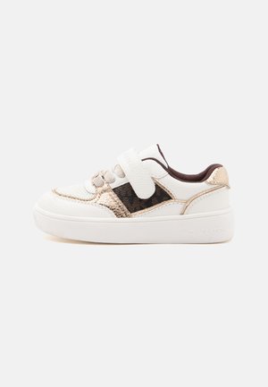 Sneaker bianca e oro metallico per bambini con strappo in velcro, pannello laterale scuro decorato e suola bianca spessa su uno sfondo chiaro e semplice.