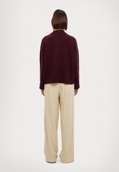 Suéter de punto burdeos con cuello acanalado, combinado con pantalones de pierna ancha de rayas en color crema y cintura alta. La textura parece suave.
