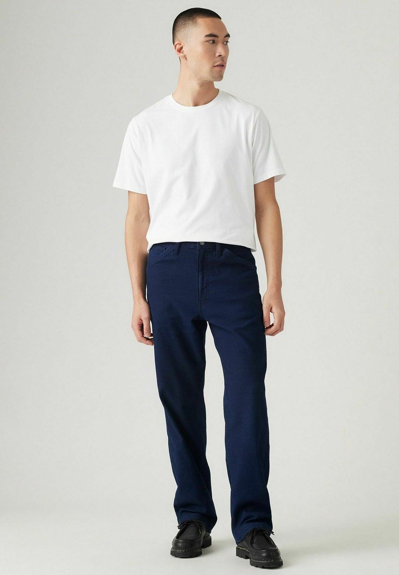 Pantalones rectos de lino azul marino, mezcla de algodón, con cierre de botón y cremallera. Combinados con una camiseta de algodón blanca sencilla y zapatos negros.