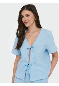 Top corto azzurro chiaro a maniche corte con scollatura a V profonda e dettagli di tie nella parte anteriore. Realizzato in tessuto testurizzato, presenta una vestibilità rilassata e cuciture sagomate.