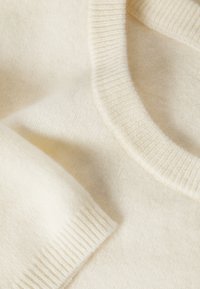 Pull en maille crème douce avec encolure ronde côtelée et détails de poignets sur un tissu en laine ou cachemire.