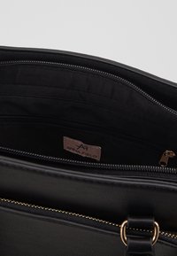 Borsa a tracolla nera con esterno in ecopelle texture, dettaglio in oro sulla cerniera e interno in tessuto nero. L'interno presenta una tasca con cerniera e un'etichetta del marchio.