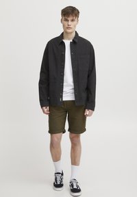 Black button-up jacket with pockets, white T-shirt, olive green rolled shorts, white socks, and black sneakers with white soles.