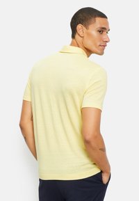 Polo shirt met korte mouwen in lichtgeel, gemaakt van een gestructureerde stof. Kenmerkt zich door een klassieke kraag en een iets getailleerd ontwerp.