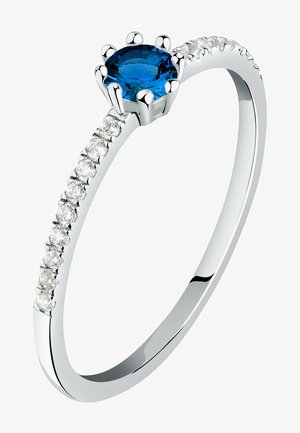 Sølvring med en central blå ædelsten i en seks-kloindstilling, med mindre klare sten langs bøljen for ekstra glans.