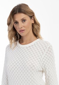 Maglione bianco lavorato a maglia con un motivo a rete testurizzato, colletto rotondo e maniche lunghe. Materiale leggero che migliora la traspirabilità.