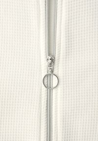 Silberner Metallreißverschluss mit rundem Zuggriff auf strukturierter weißer Stofffläche, zentriert und vollständig geschlossen.