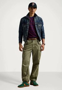 Džinsinė striukė, dryžuota tamsiai mėlyna ir raudona marškinėliai, alyvuogių spalvos krepšių kelnės su kišenėmis, žali sportbačiai su oranžiniais akcentais, juoda kepurė. Kasdienis drabužių derinys.