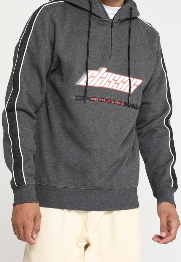 Sweat à capuche gris foncé avec le texte "classic" sur le devant, détails rayés noirs et blancs sur les manches, porté avec un pantalon de couleur claire.