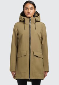 Khaki nepremokavá parka s kapucňou, čierny zips, dve predné vrecká a rovný strih. Hladká tkanina s matným povrchom.