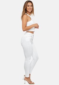 Jeans ajustados blancos con una textura suave, complementados por una blusa de tirantes blanca corta. Sandalias de tacón alto transparentes completan el conjunto.