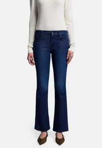 Jeans in denim blu scuro a vita alta con gamba svasata, dotati di tasche anteriori e una leggera sfumatura. Abbinati a un maglione crema e scarpe con stampa animale.