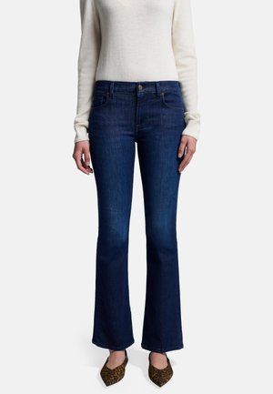 Jeans en denim bleu foncé évasés avec une taille haute, présentant des poches avant et un léger dégradé. Associés à un pull crème et des chaussures à imprimé animal.