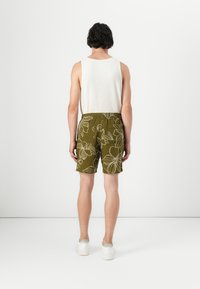 Mandens olivengrønne shorts med hvide blomster mønstre, elastisk talje og afslappet pasform, parret med en ensfarvet hvid tank top og hvide sneakers.