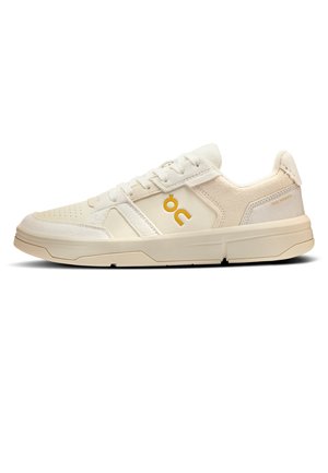 Off-white low-top sneaker with suede and leather panels, beige sole, lace-up closure, and yellow "OC" logo on the side.