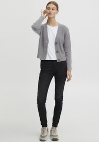 Grå ribbestrikket cardigan med tre tresknapper, brukt over en hvit t-skjorte, sammen med svarte skinny jeans og lyse grå joggesko.