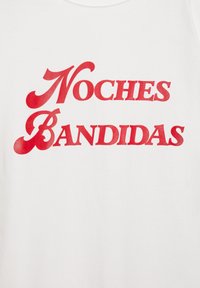 Biely textilný tričko s výrazným červeným textom "Noches Bandidas" v dekoratívnom písmene, zdôrazňujúce hladkú textúru a jasnú čitateľnosť.