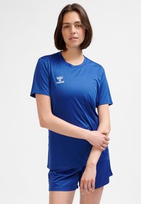 Niebieska sportowa koszulka i szorty wykonane z gładkiej tkaniny. Koszulka ma krótkie rękawy i okrągły dekolt, z białym logo na piersi.